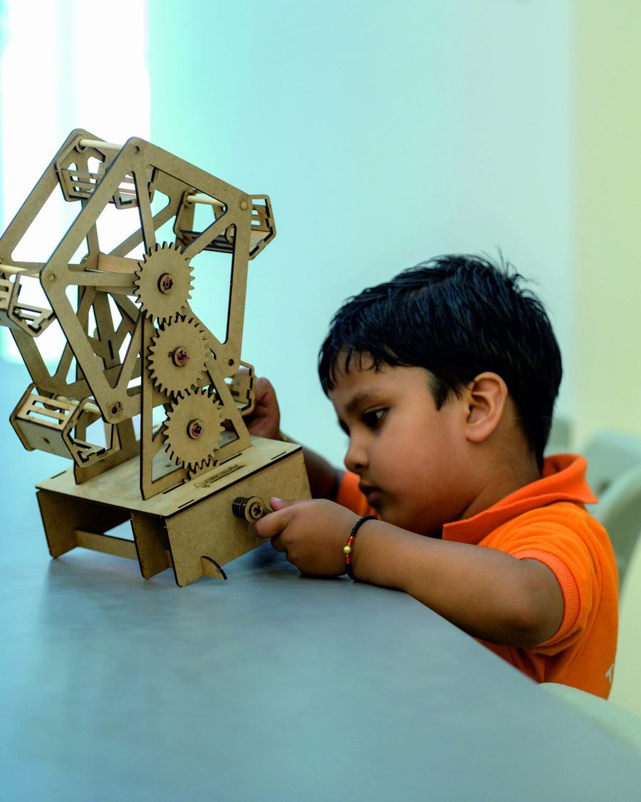 A student assembling the gears of a wooden Ferris wheel model