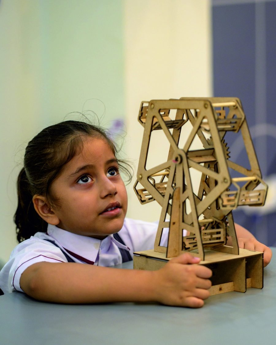 A student examining a wooden Ferris wheel model in the maker lab